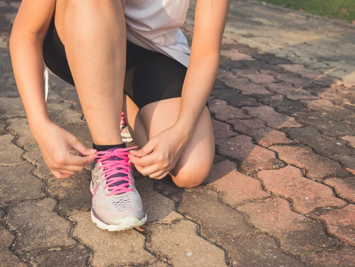 woman tying tennis shoes on walking path