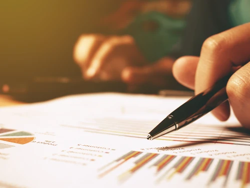 someone holding a pen over graphs on a paper