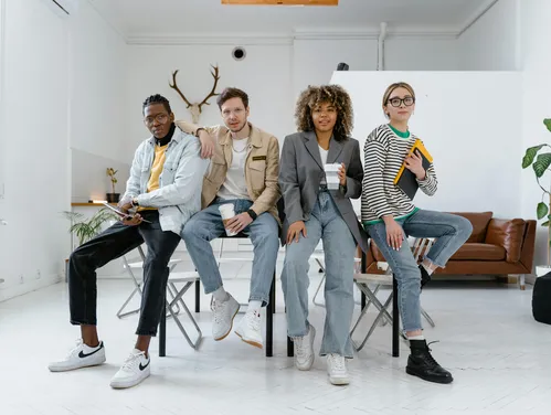 group of four young adults sitting in an office space with coffees and notebooks