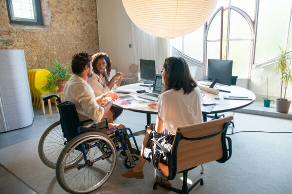 Group of workers sitting around a table, two in chairs, one in a wheelchair