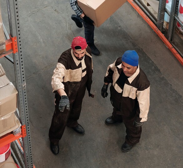 Two men in a warehouse one pointing to something helping the other