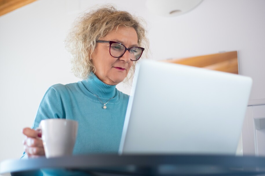 Mature woman with coffee looking at laptop