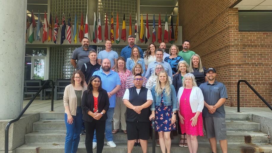 Photo of 22 people standing on concrete steps with flags behind them.