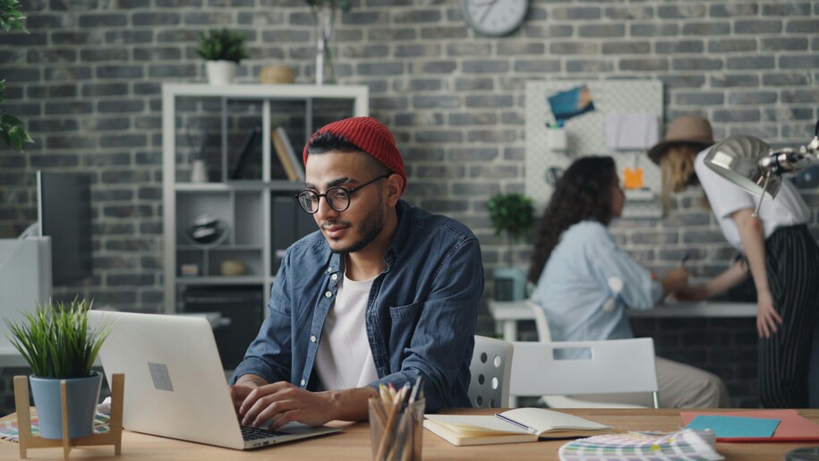 Young Man wearing a red Hat at laptop in casual office setting