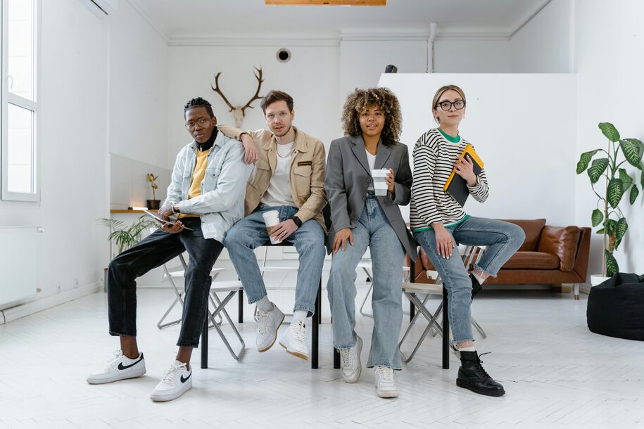 group of four young adults sitting in an office space with coffees and notebooks